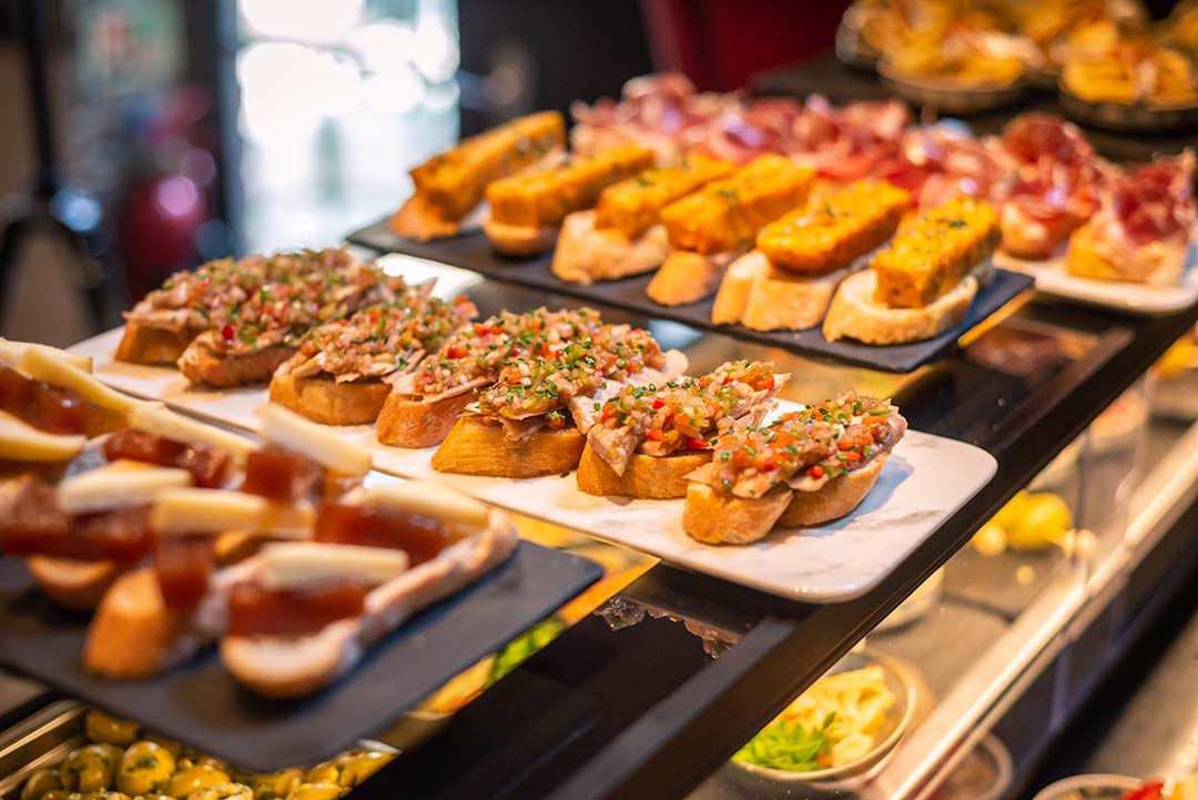 A selection of pinchos featuring a slice of Spanish tortilla on thinly sliced bread, tuna mixed with fresh herbs and chopped chilli on sliced bread and cheese on crustini.