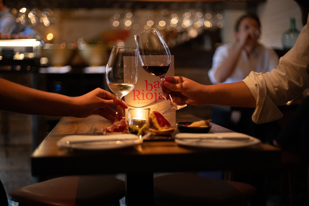 Two people cheersing wine glasses over a table